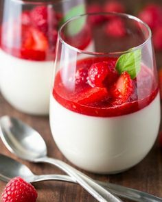 two glasses filled with yogurt and strawberries next to some raspberries