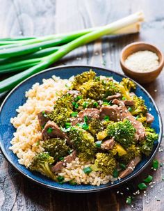 a blue plate topped with rice and broccoli covered in sauce next to green onions