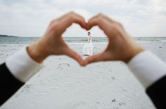 a person making a heart shape with their hands on the beach in front of them