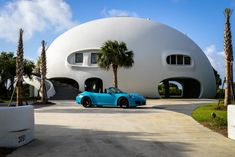 a blue sports car parked in front of a round house