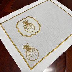 a white table cloth with gold trimmings and ornaments on the edges, sitting on a wooden surface