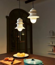 three lights hanging from the ceiling above a table with plates and oranges on it