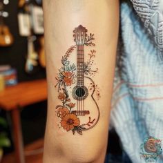 a tattoo on the arm of a woman with an acoustic guitar and flowers around it