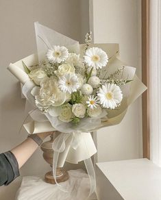 a bouquet of white flowers sitting on top of a table next to a person's hand