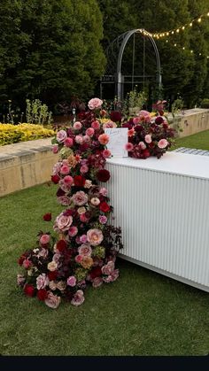 a white box with flowers on it sitting in the grass next to a flower garden