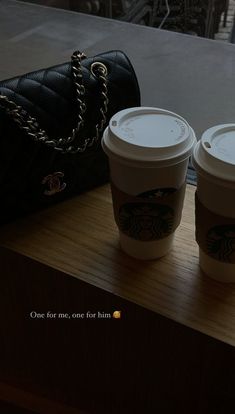 two cups of coffee sitting on top of a wooden table next to a handbag