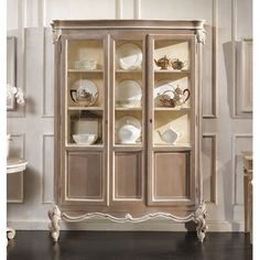 an antique china cabinet with glass doors and plates on it's shelves, in front of a white wall