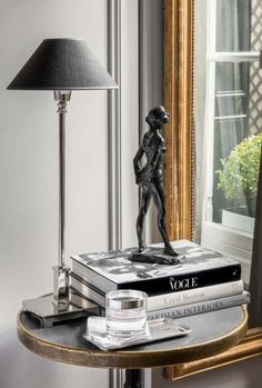 a table with a lamp, books and a statue on it in front of a mirror