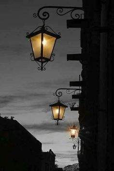 two street lamps hanging from the side of a building at night with clouds in the background