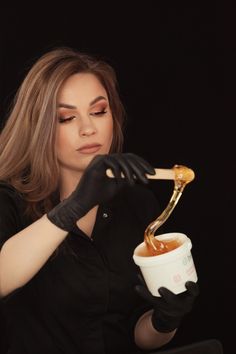 a woman in black gloves is holding a cup and spoon with honey dripping out of it