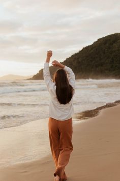 a woman walking on the beach with her arms in the air