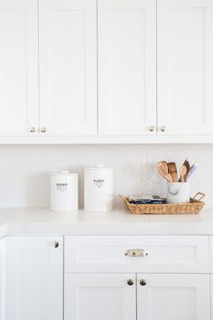 white kitchen cabinets with wooden utensils in the basket and two mugs on the counter