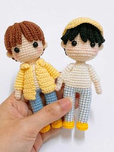 two tiny knitted dolls are being held by a hand