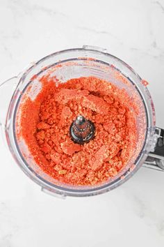 an overhead view of a blender filled with red food and seasoning on a marble counter top