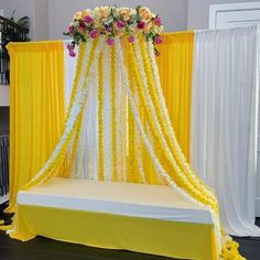 a yellow and white wedding setup with flowers on the headboard, draping and curtains