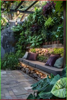 an outdoor seating area with lots of plants on the wall and stone flooring around it