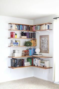 a corner book shelf filled with lots of books next to a white wall and window