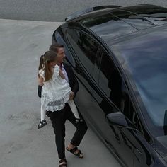 a man and woman walking next to a black car