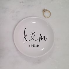 a white plate with the word k & m on it and a wedding ring laying next to it