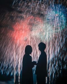 two people standing next to each other with fireworks in the background