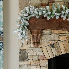 a stone fireplace with snow on the mantle and pine branches hanging from it's mantel