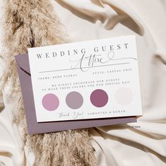 a wedding guest card sitting on top of a white sheet with pink and purple circles