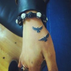 a woman's hand with two birds tattooed on the left side of her wrist