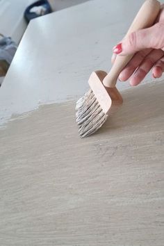 a person holding a brush on top of a piece of plywood paper with wood shavings