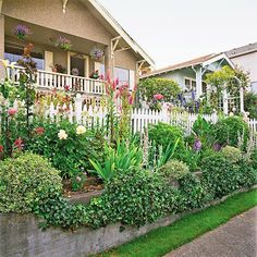 a house with lots of flowers in the front yard and landscaping on the side walk