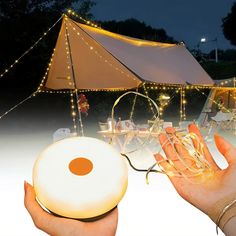 a hand holding an object in front of a tent with string lights and fairy lights