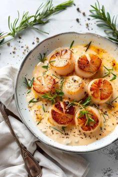 a white bowl filled with scallops covered in sauce and garnished with herbs