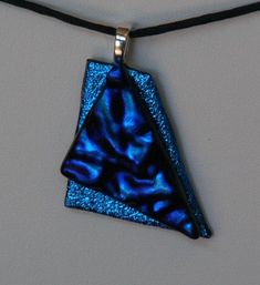 a blue necklace with a triangle shaped glass piece hanging from it's back end