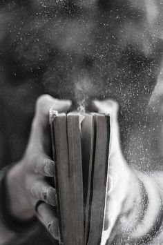 a person holding an open book in their hand with dust coming out of the pages