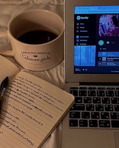 a laptop computer sitting on top of a bed next to a cup of coffee and notebook