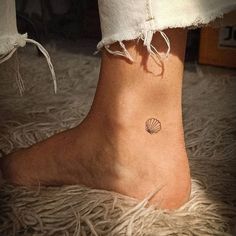 a woman's foot with a small shell tattoo on the side of her ankle