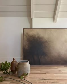 a vase sitting on top of a hard wood floor next to a painting and potted plant