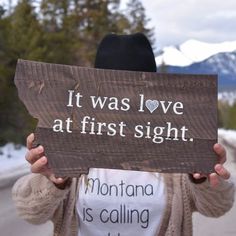 a woman holding up a wooden sign that says it was love at first sight montana is calling idaho