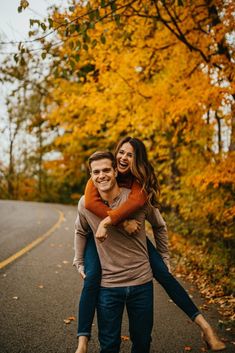 a man carrying a woman on his back while walking down the road in front of trees