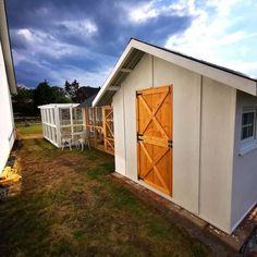 two sheds with wooden doors and windows in the grass next to each other on a cloudy day