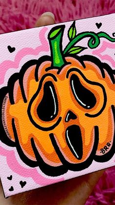 a hand holding up a small card with a cartoon pumpkin on it's face