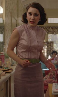 a woman in a pink dress is standing near a counter and looking at the camera