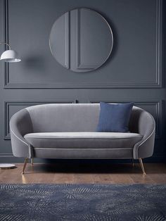 a living room with grey walls and blue rugs on the floor, a round mirror above the couch