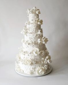 a three tiered white wedding cake with flowers on the top and bottom, sitting on a plate