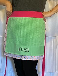 a person wearing an apron with the words he is risen printed on it, while standing in front of a white curtain