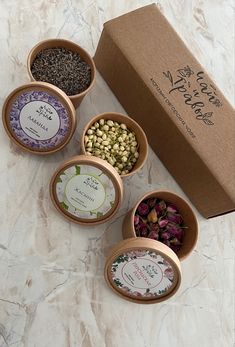 four small bowls filled with different types of spices next to a brown box on a marble surface