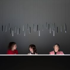 three women are sitting at a table in front of a wall with lights hanging from it