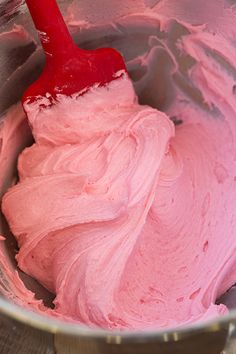 a red spatula in a metal bowl filled with pink icing