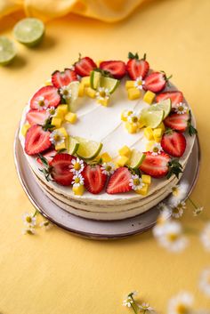 a cake decorated with strawberries and limes on a yellow tablecloth next to flowers