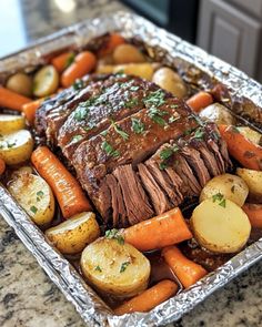 a roast beef with carrots and potatoes on a tin foil tray in the kitchen