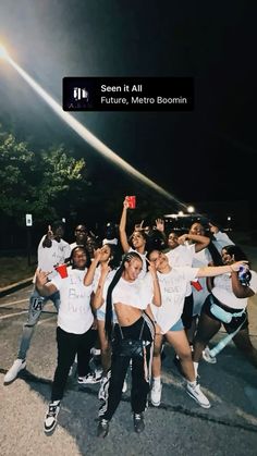 a group of young people standing next to each other on a street at night with their arms in the air